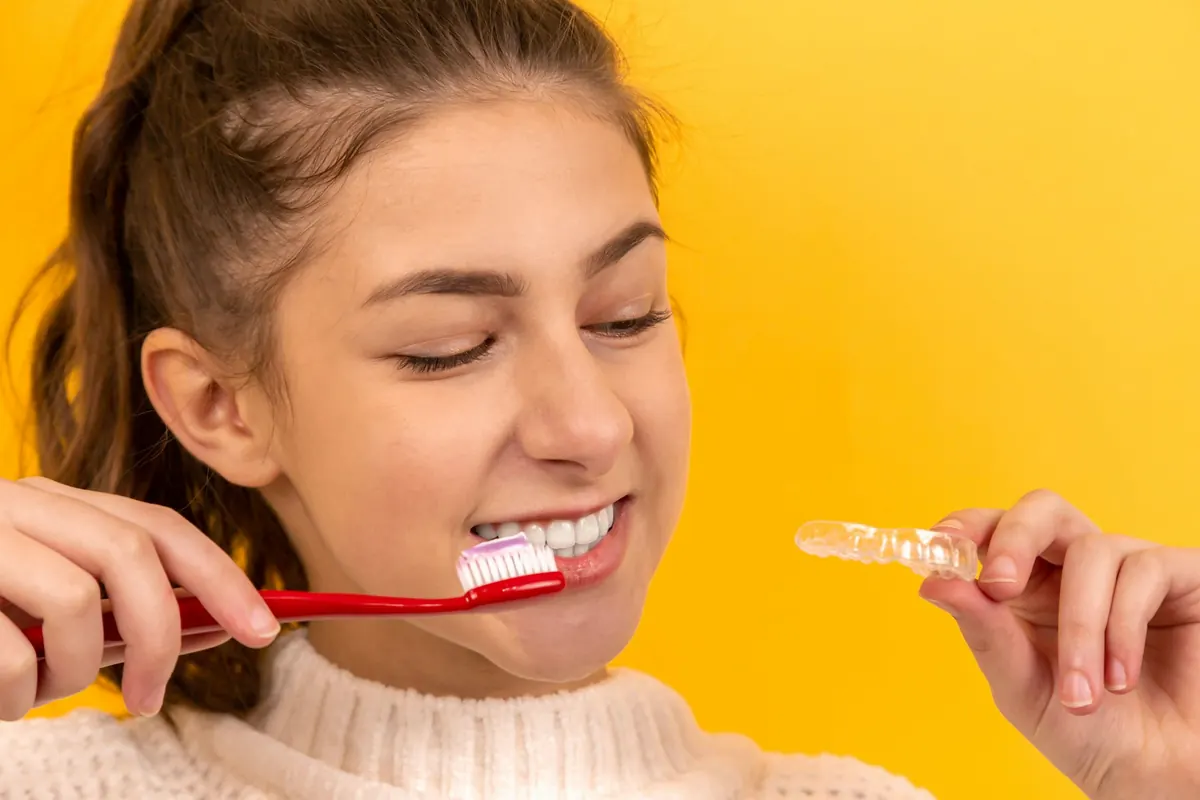 Teen brushing her teeth while holding her clear aligner